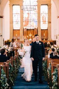 bride and groom walking down the aisle in church , pew end decorated with trailing foliage